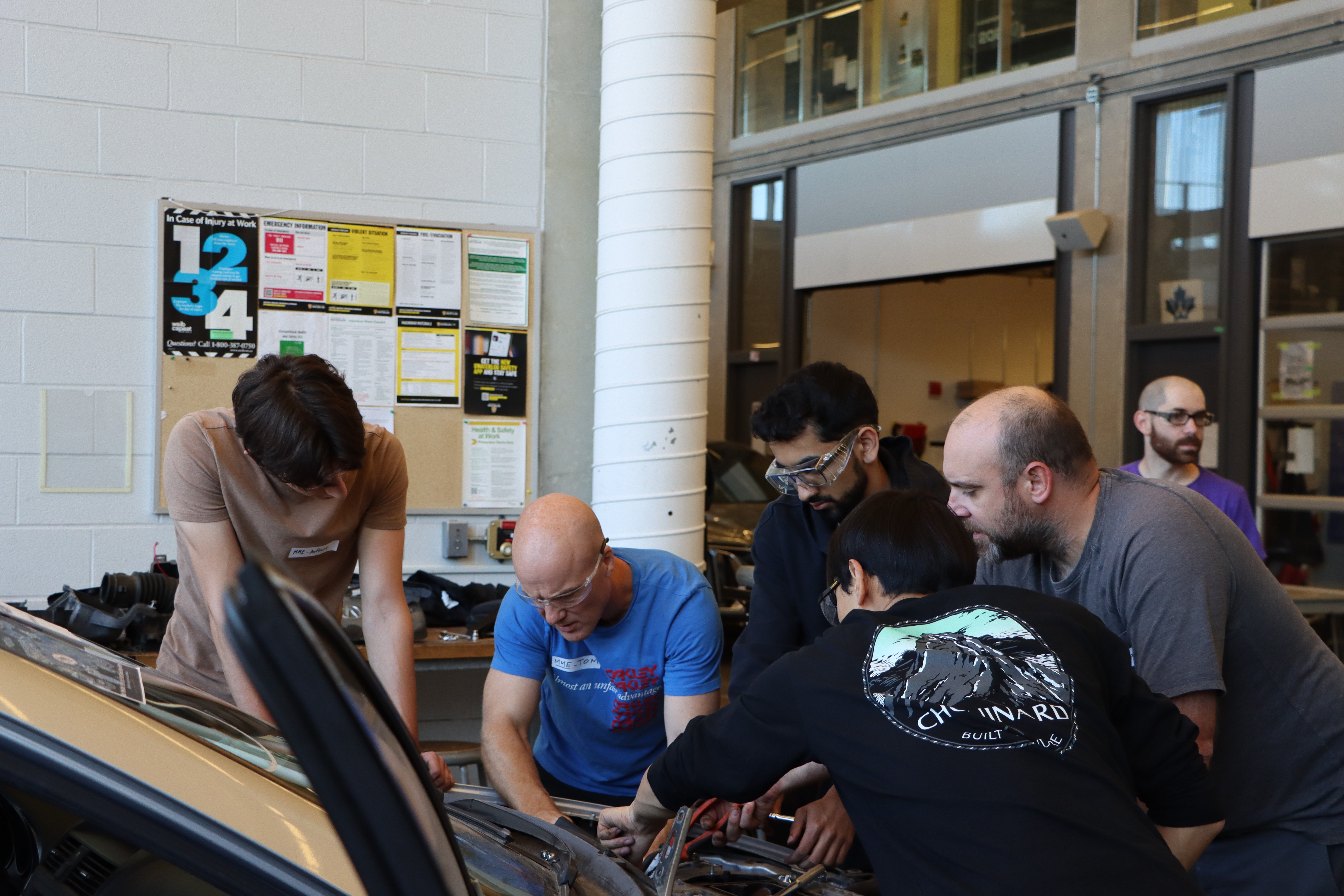 Students examining underneath the hood of a car. 