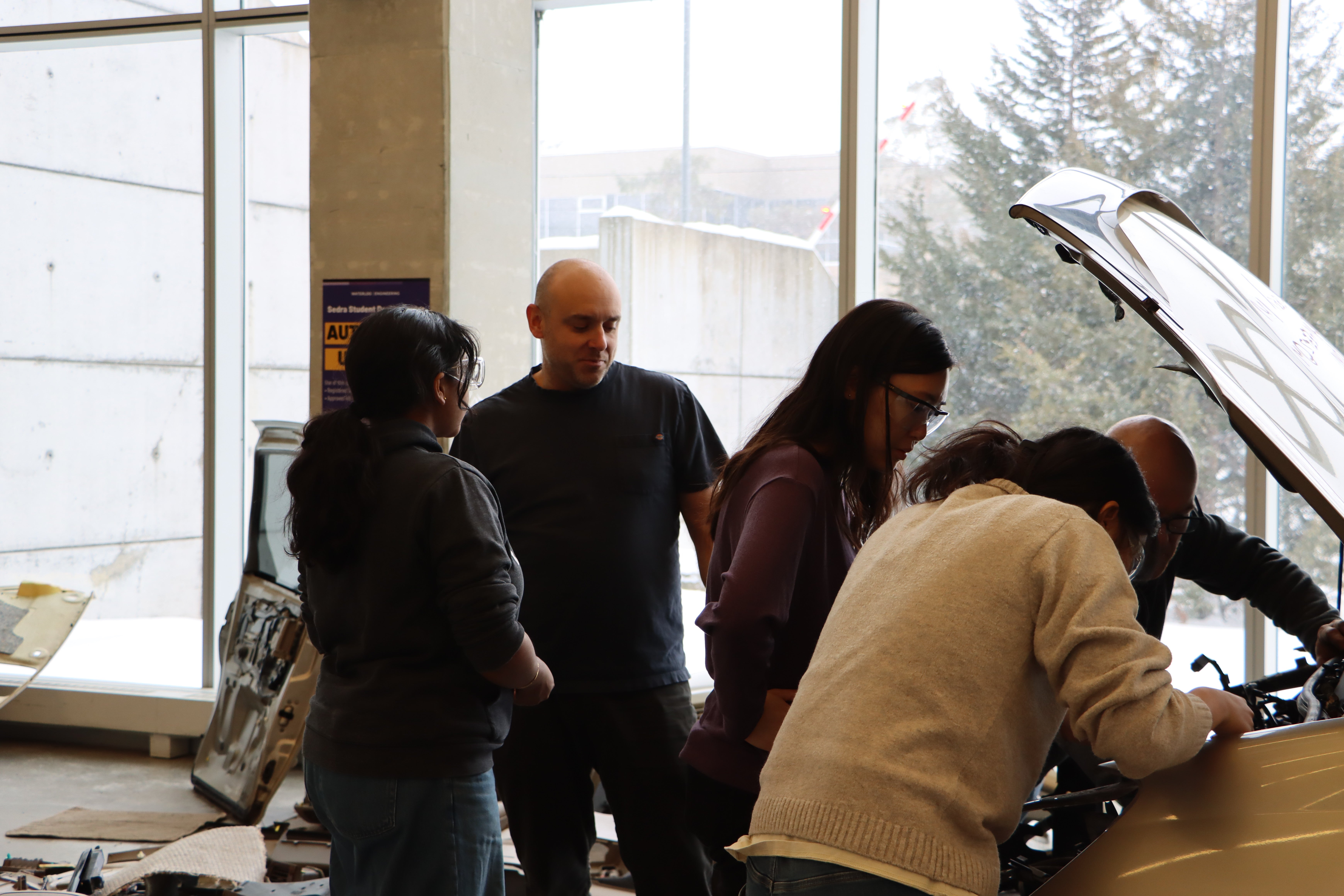 Students working underneath the hood of a minivan. 