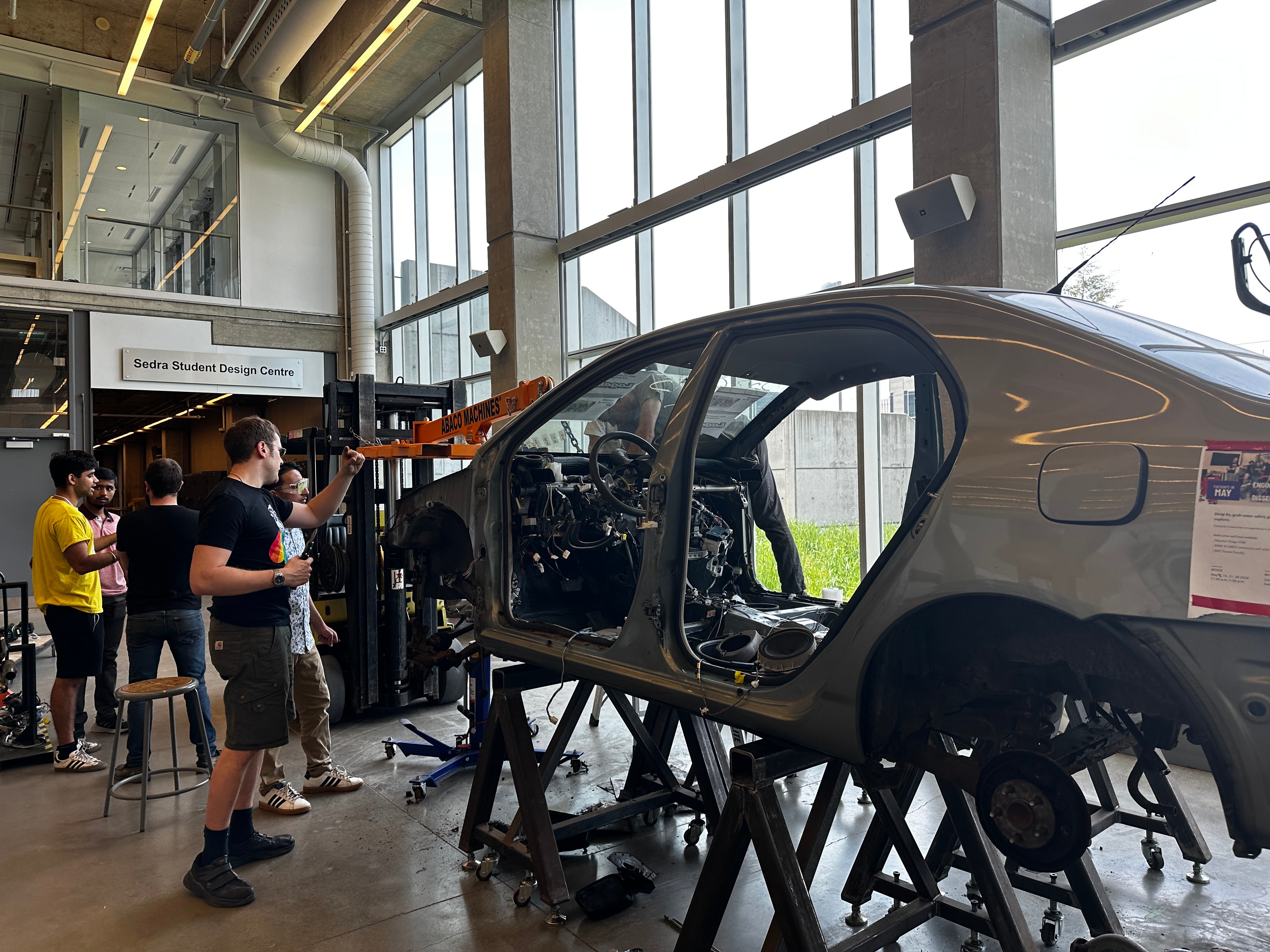 Stripped down car with students working on it in the background
