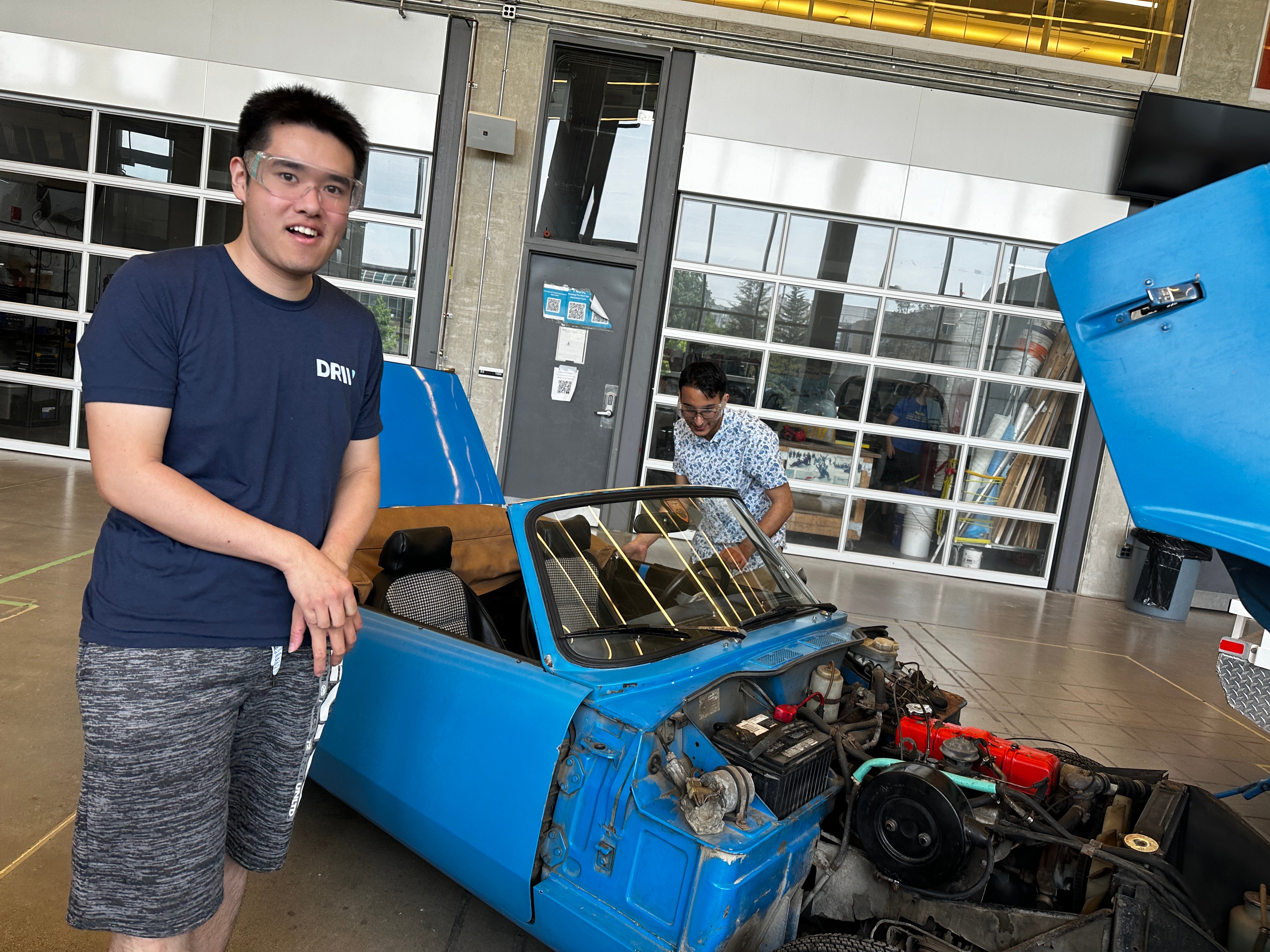 2 students standing with an older vehicle