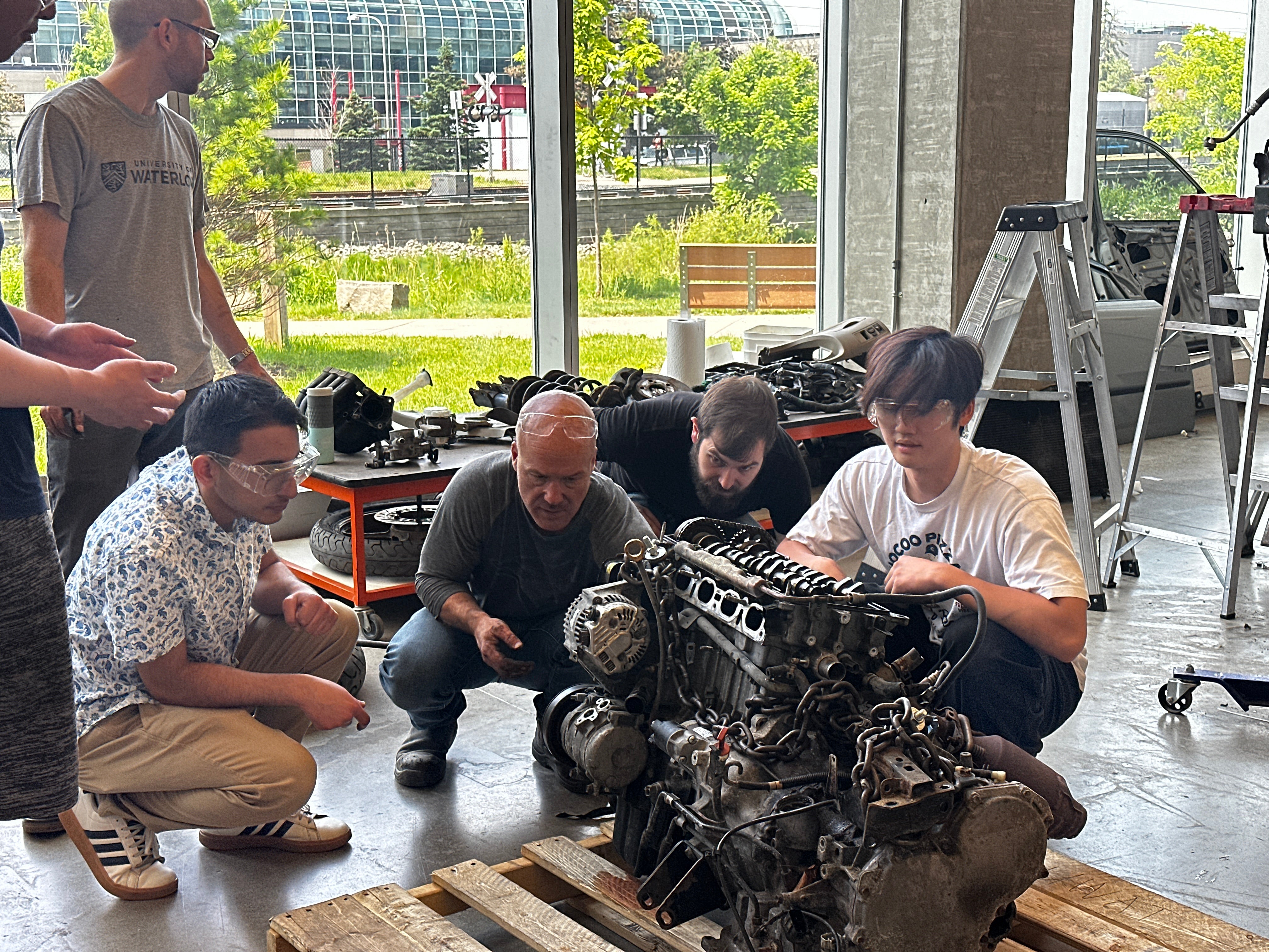 Students and staff examining a car engine. 