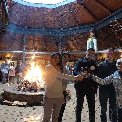 Four people clinking beer bottles in front of a bonfire