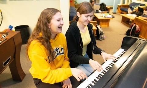 two students sitting together playing piano