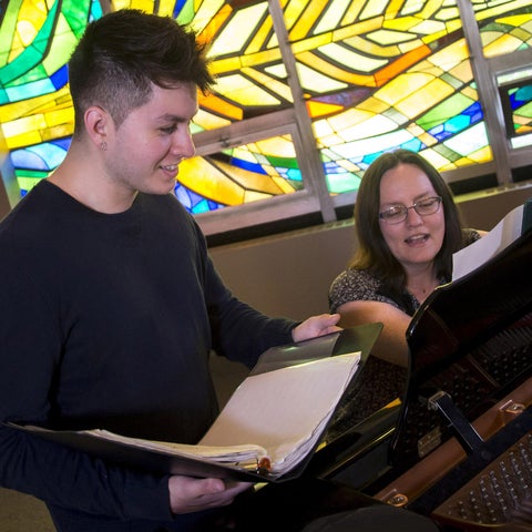student and professor sitting by a piano in the chapel