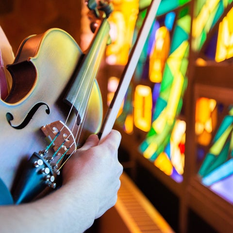 A student holds a violin in front of the colourful chapel stainglass windows.