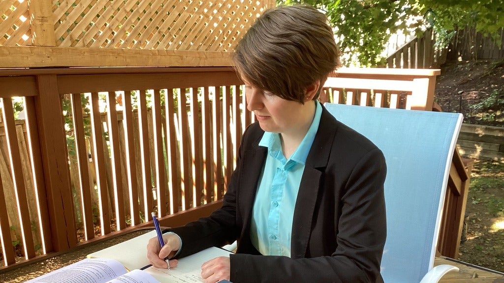 Marina Gallagher writing in a notebook at a table outside