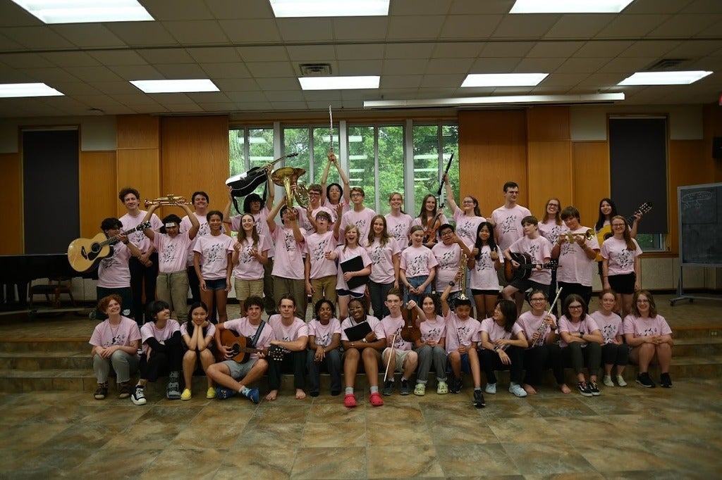 Big group of young students posing for a group photo in pink OMMC shirts with their instruments