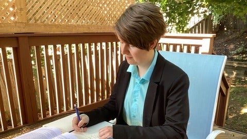 Marina Gallagher writing in a notebook at a table outside