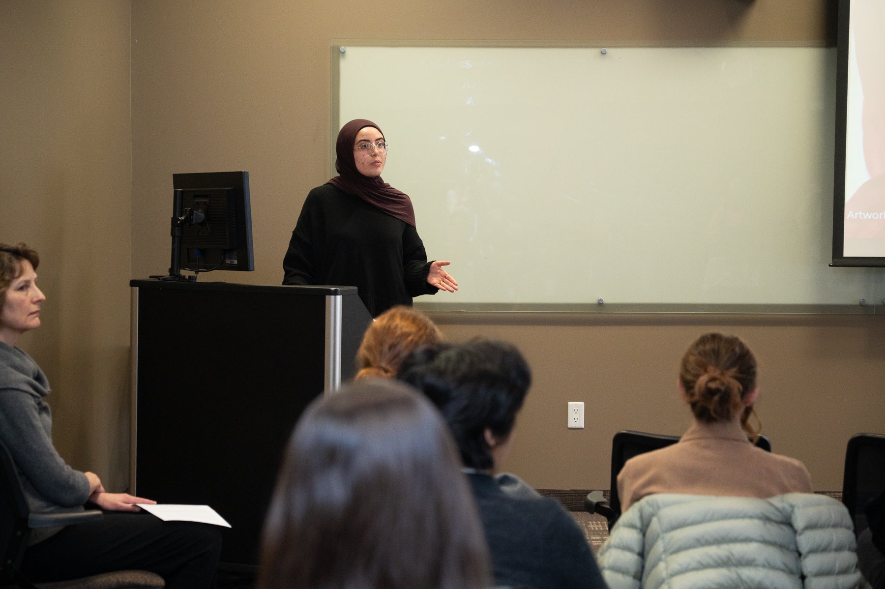 Salma Aldeeb presenting standing at podium in front of a crowd