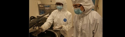 Two students in clean room suits working in the lab