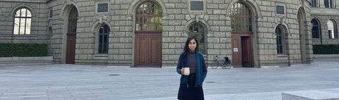 a woman with black hair holding a coffee cup in front of a brick building