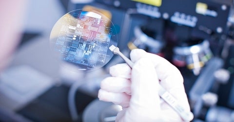 hand in white gloves holding a intergrated chip with pincers