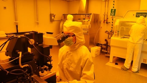 lab tech looking through microscope in clean room