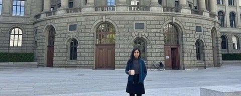 a woman with black hair holding a coffee cup in front of a brick building