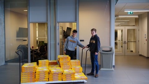 Two students pose with stacks of pizzas before the Meet the Professor event.