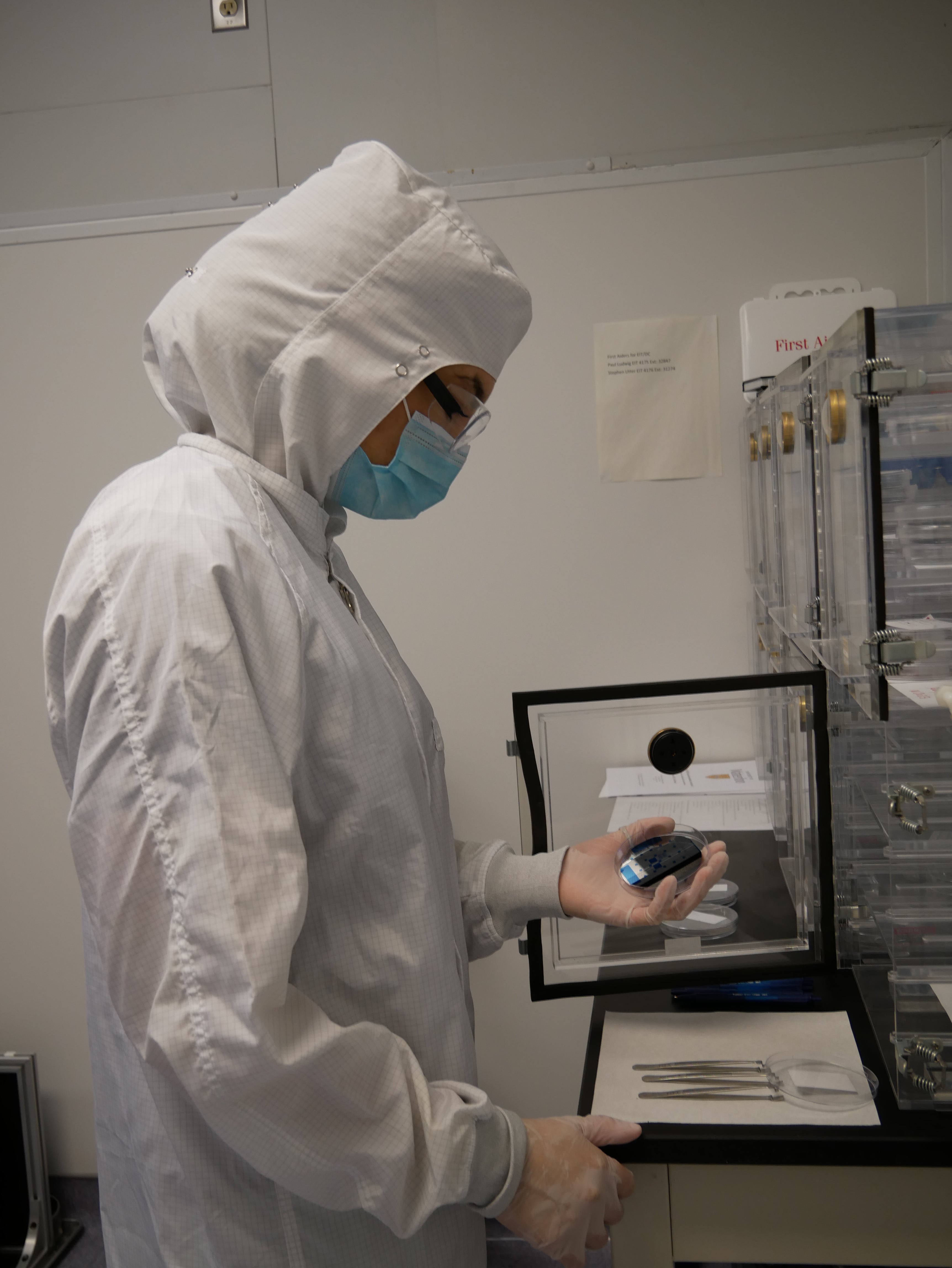 Technician in clearoom suit looking at a wafer