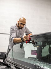 a bald man with a beard and glasses scrapping a windshield