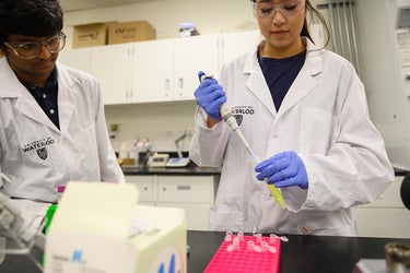a man and a woman in lab coats, safety glasses and blue gloves