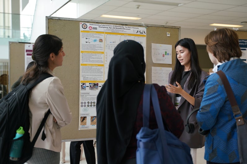 A student presents their poster to a group at the Symposium on Aging Research 2025.