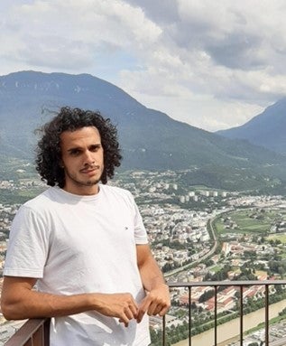 A medium close-up of Arthur Eduardo Casagrande Pinto on a balcony, with a mountainous landscape and city in the background.