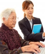 Elderly woman using a computer, with assistance from young woman.