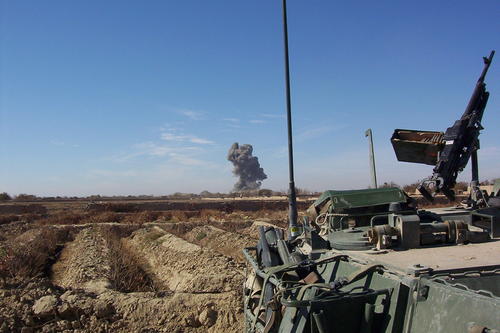 field with a tank and smoke in the background