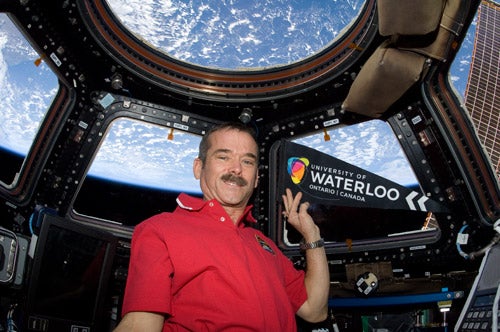 Chris Hadfield holding University of Waterloo pennant in space