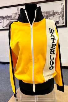 Front view of a yellow tracksuit jacket with black stripes down the sleeves and Waterloo pressed vertically on the front