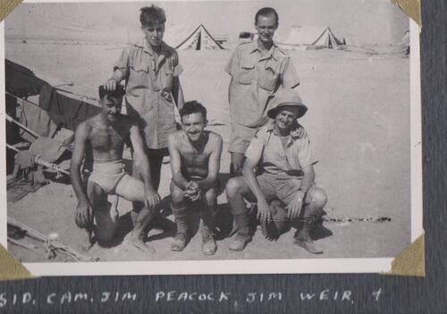 a black and white photo of five men in a desert with tents in the background