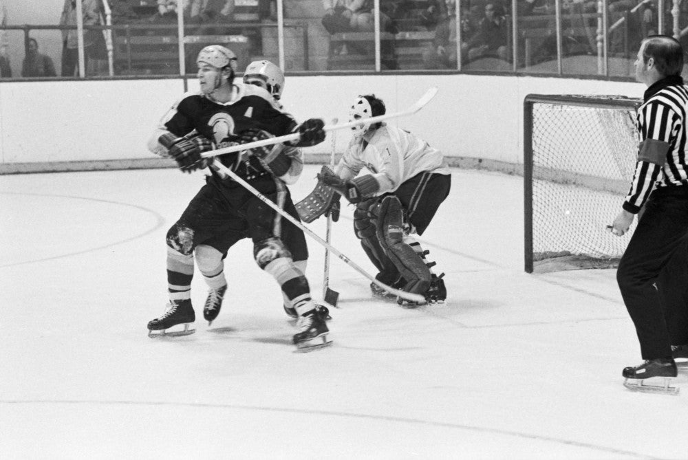 Black and white photo two hockey players jostling in front of the goalie's net