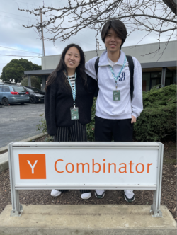 Two students stand in front of a sign at the Y Combinator