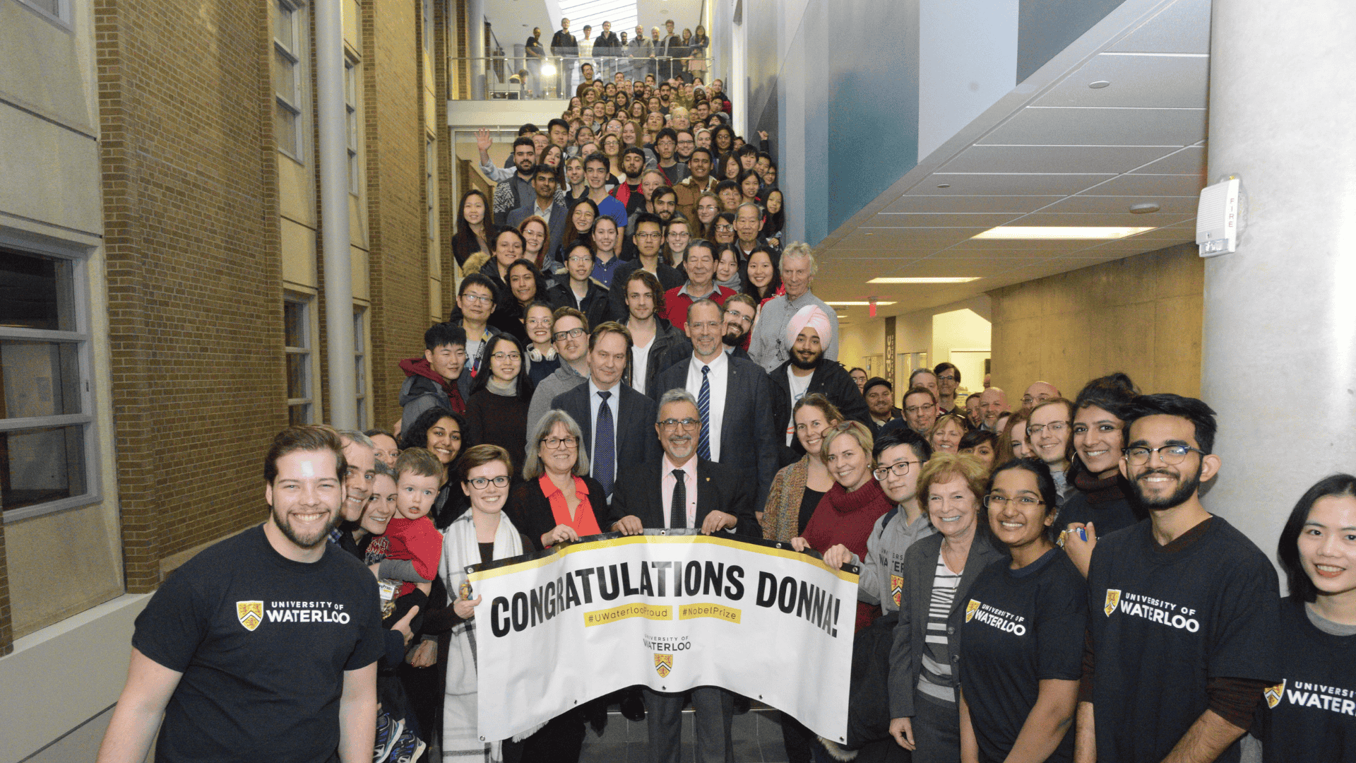 A large group of people gathered on a stairwell holding a “Congratulations Donna” banner at a University of Waterloo celebration