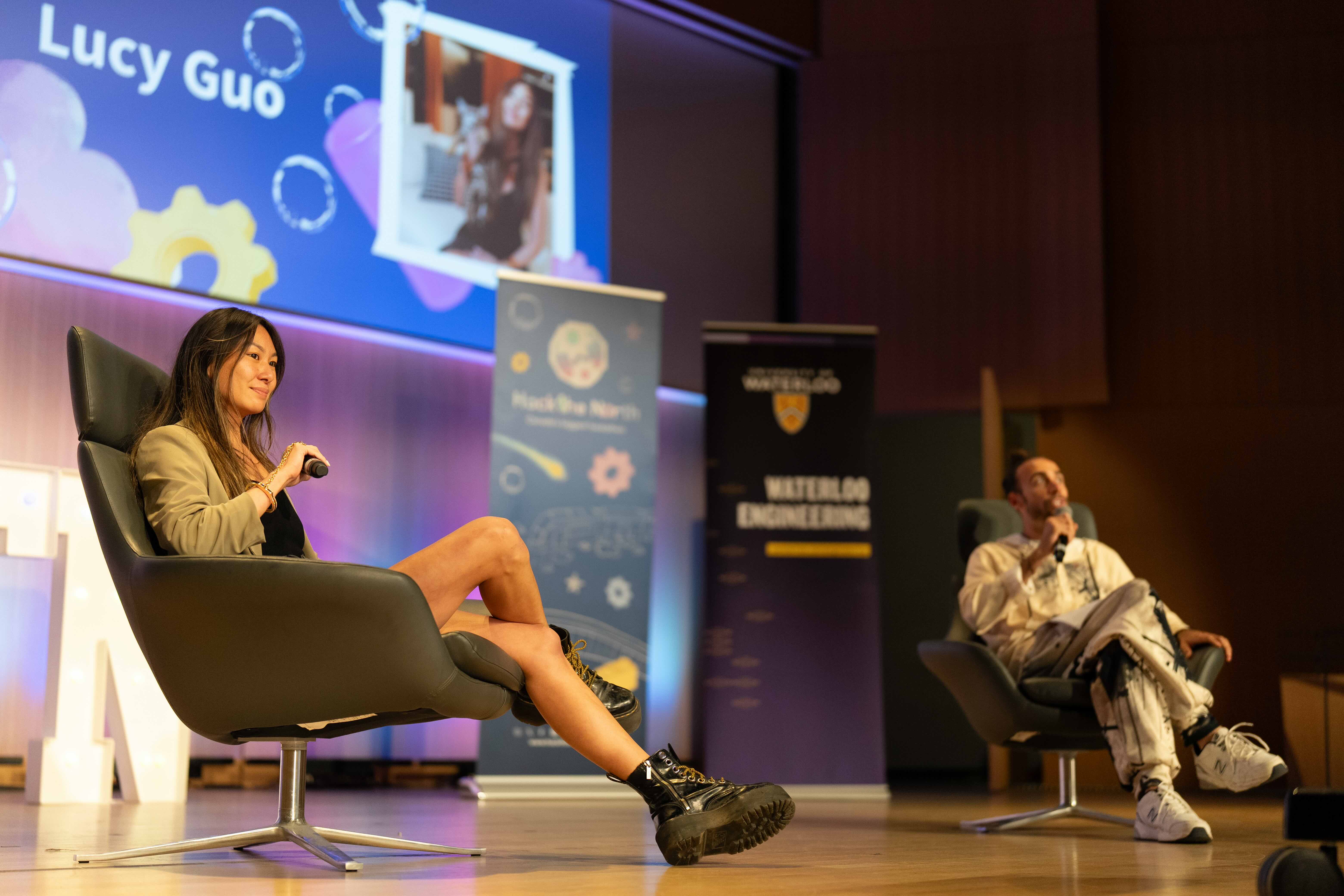 Lucy Guo sits in a chair holding a microphone during a keynote address