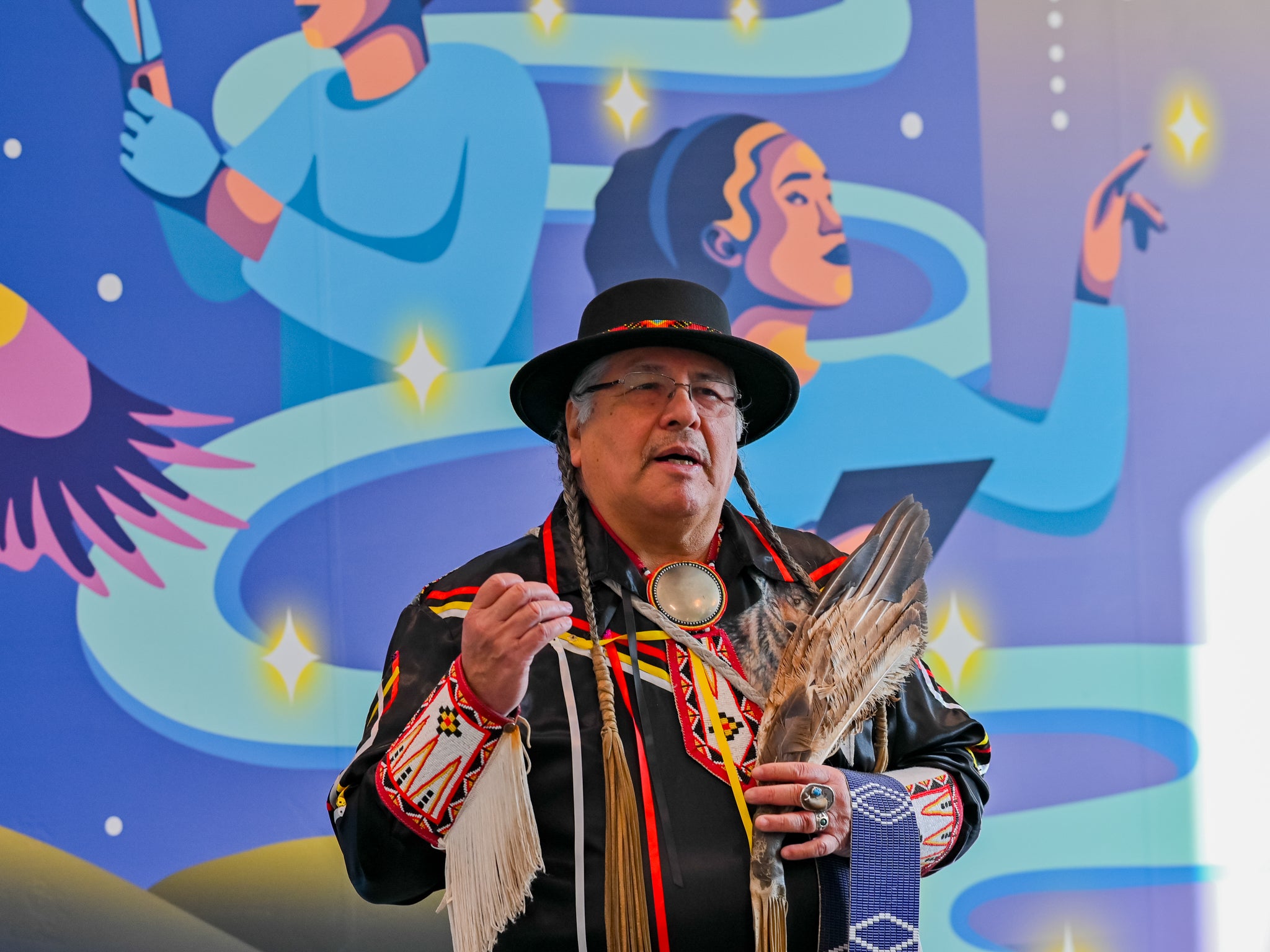 Elder Myeengun Henry holding a Wampum Belt and speaking inside the Innovation Arena