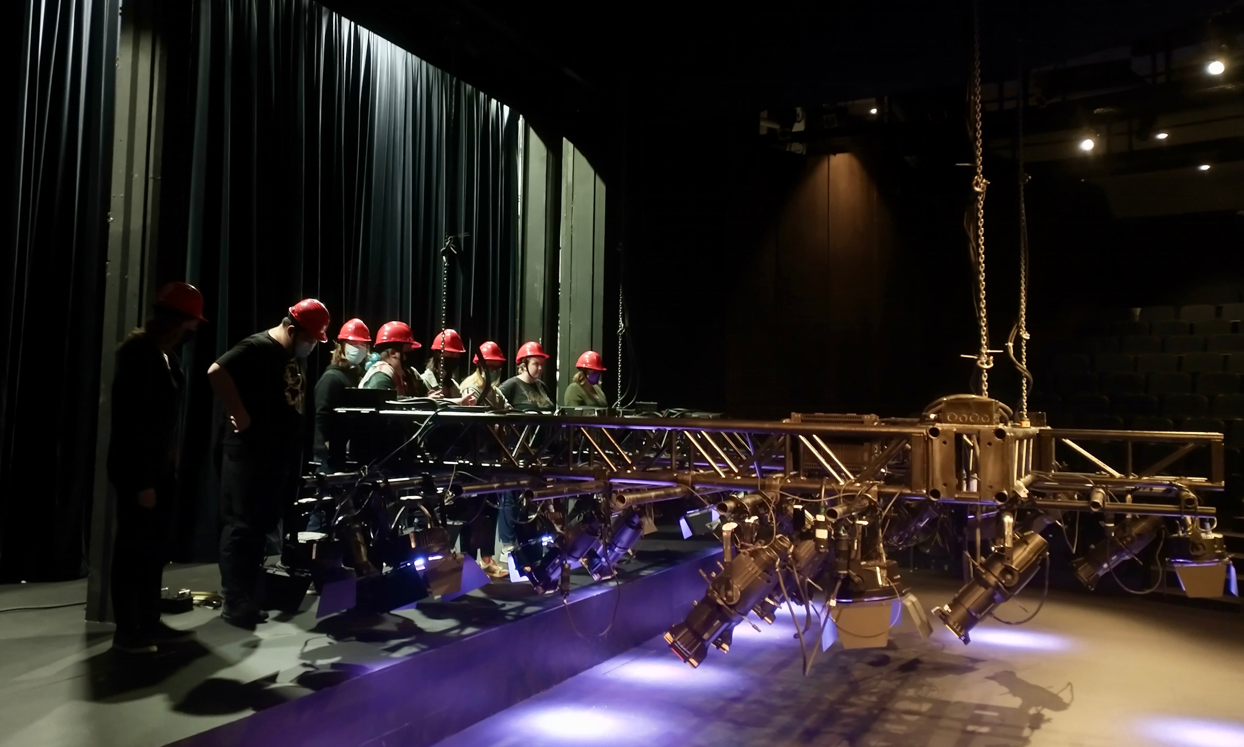 Row of students in hardhat raising the stage lighting grid