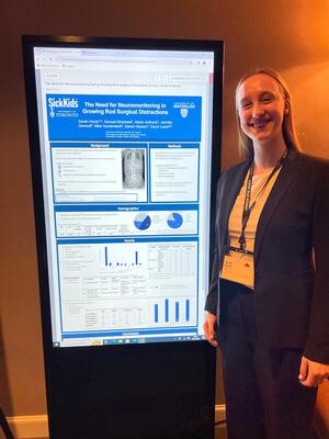 Sarah Hardy standing next to a digital poster that presents SickKids research.