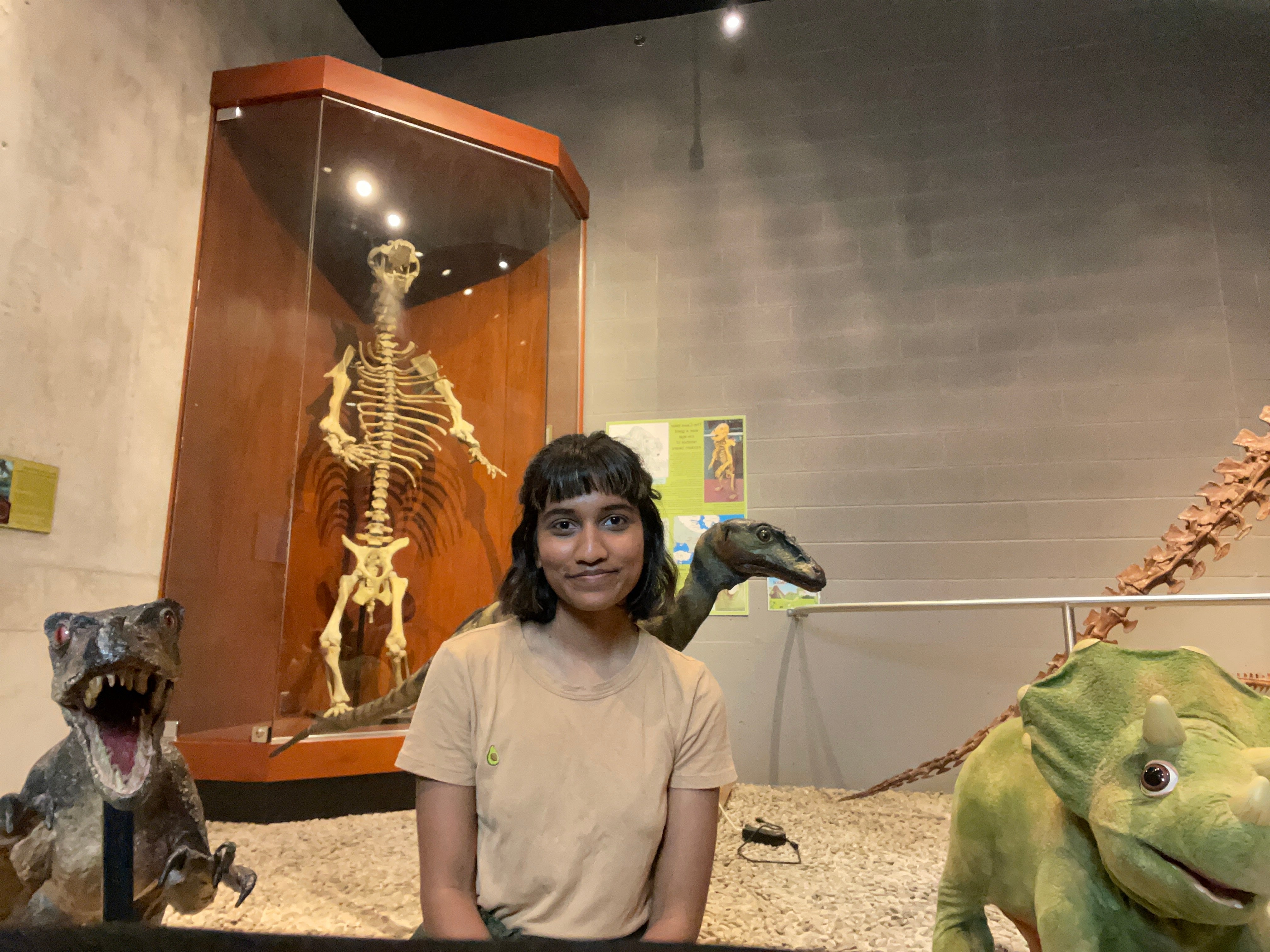 Sana Ahmad sitting in front of a dinosaur display at The Museum