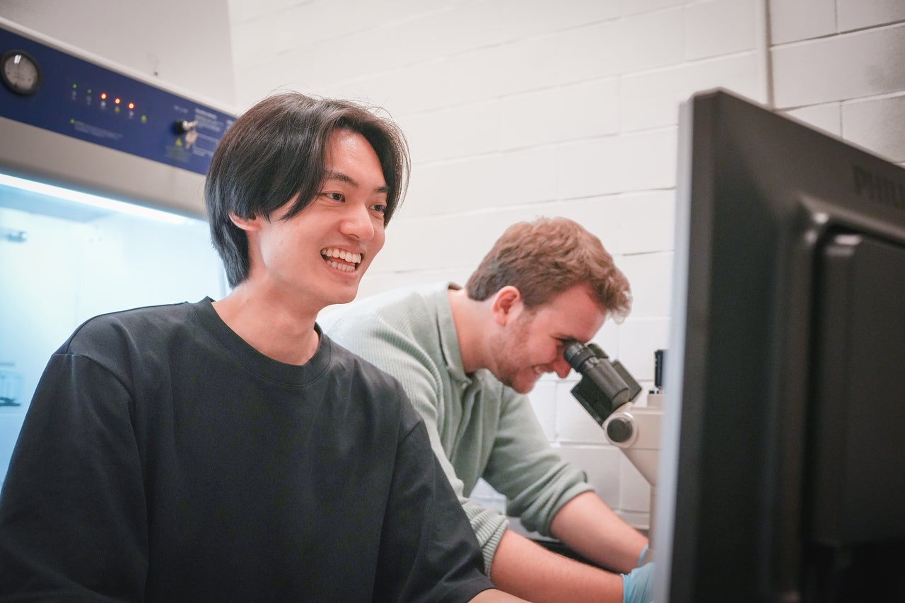 On the left Kevin Shen is looking at the computer. On the right Rikard Saqe is looking through a microscope.