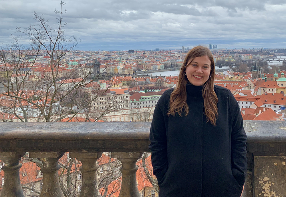 Mackenzie stands on a balcony overlooking the red roofs of Prague