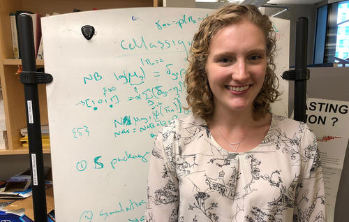 Pascale Walters smiles at the camera as she stands in front of a white board with mathematic equations on it.