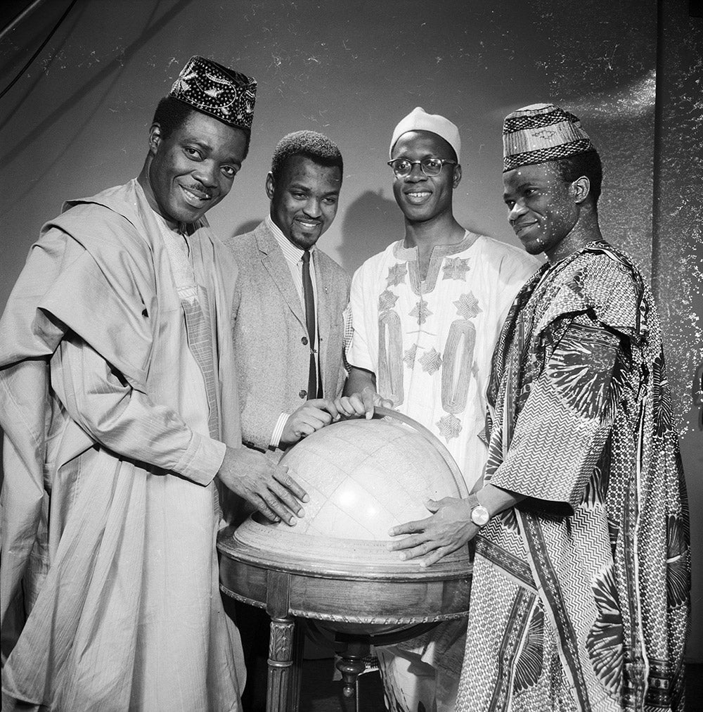 Four Nigerian students in traditional dress with their hands on a large globe