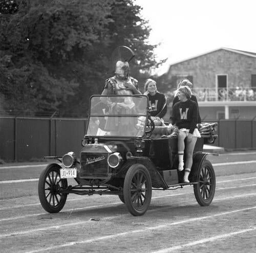 Students ride in an old car with Waterloo's mascot, the Spartan.