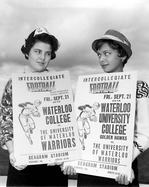 Young women hold signs advertising a football game between UW and WUC, circa 1962