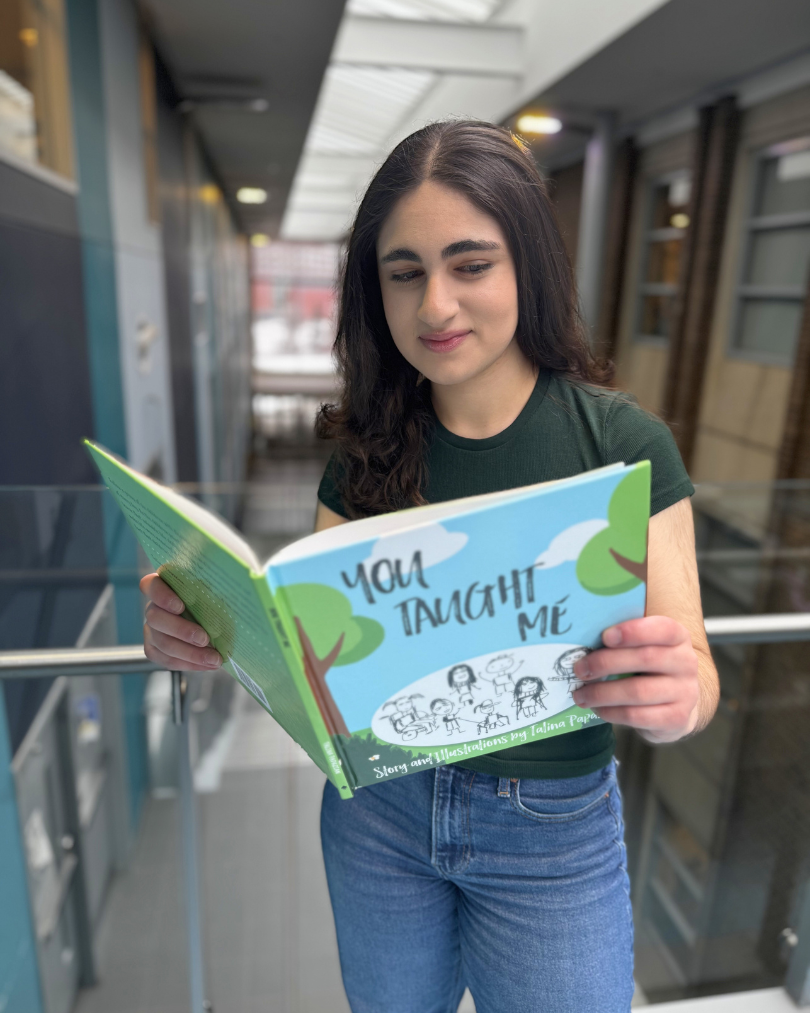 Talina Papazian holding open her book, You Taught Me, and reading it in the Science Teaching Complex.