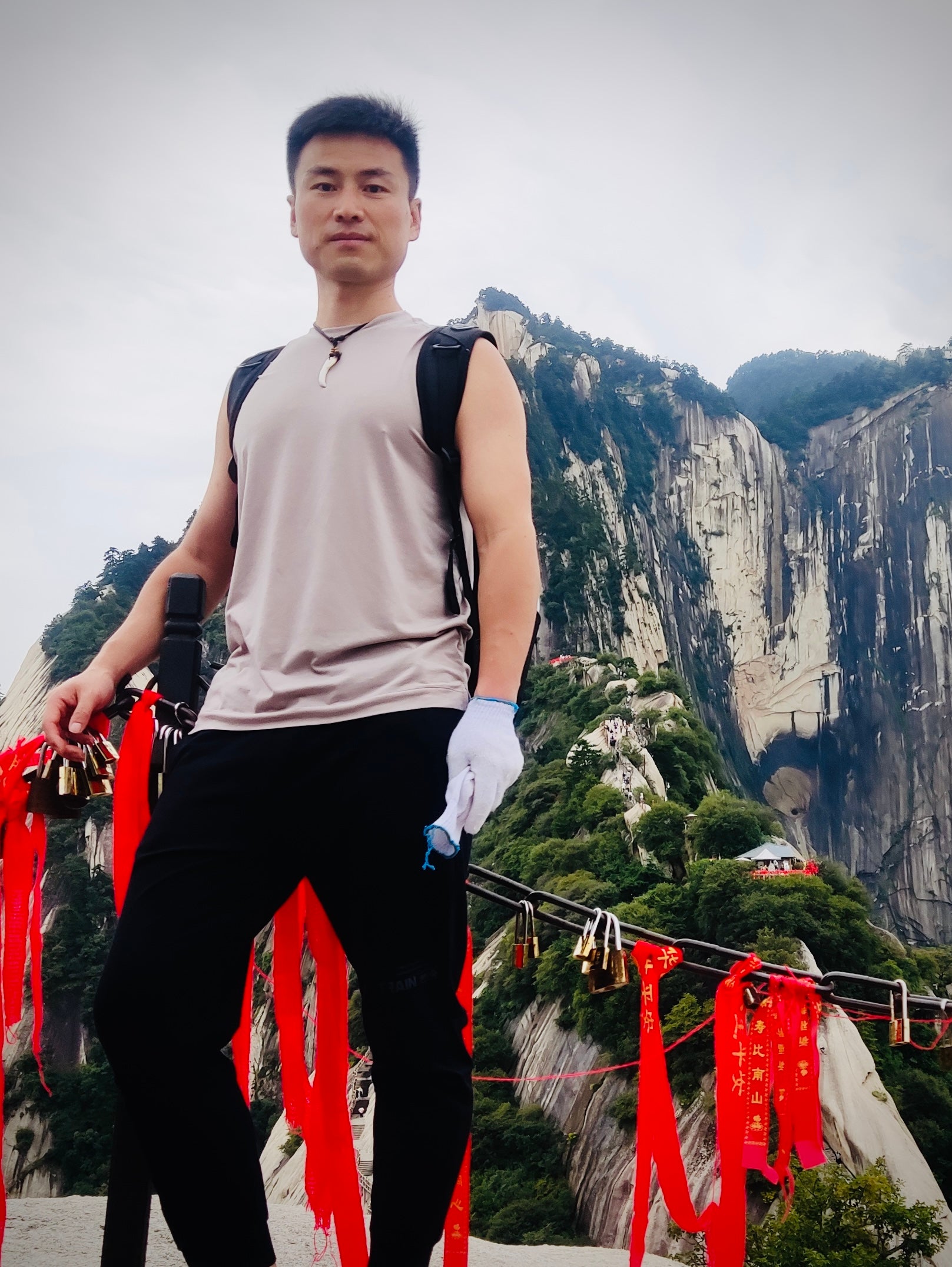 Tao Guo wearing beige shirt and black pants while standing on top a mountain