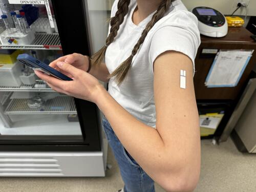 woman wears painless patch on left arm and holds a smartphone
