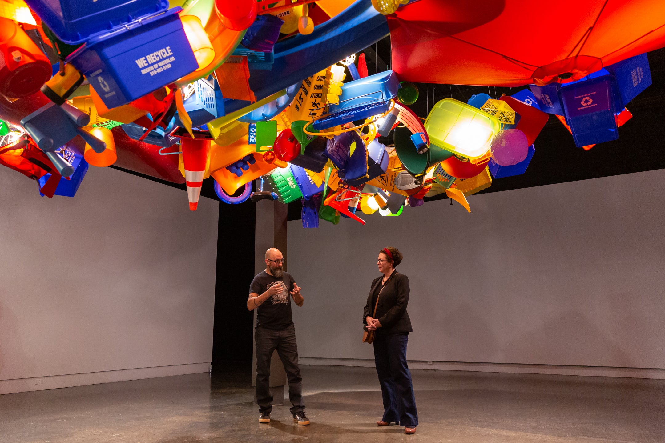 two people talking in gallery with giant art installation above their heads