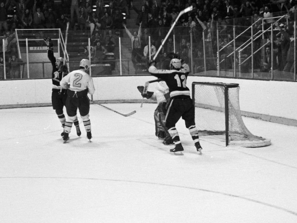 Black and white photo of hockey players raising their sticks after scoring a winning goal