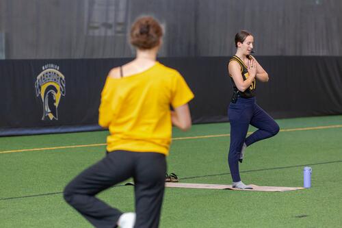 A yoga instructor and participant stand on one leg in tree pose