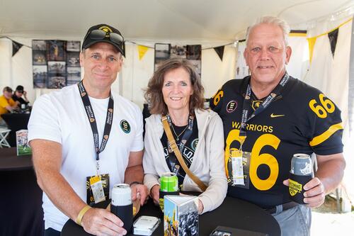 Alumni stand together in a tent, one wearing his football jersey from Waterloo